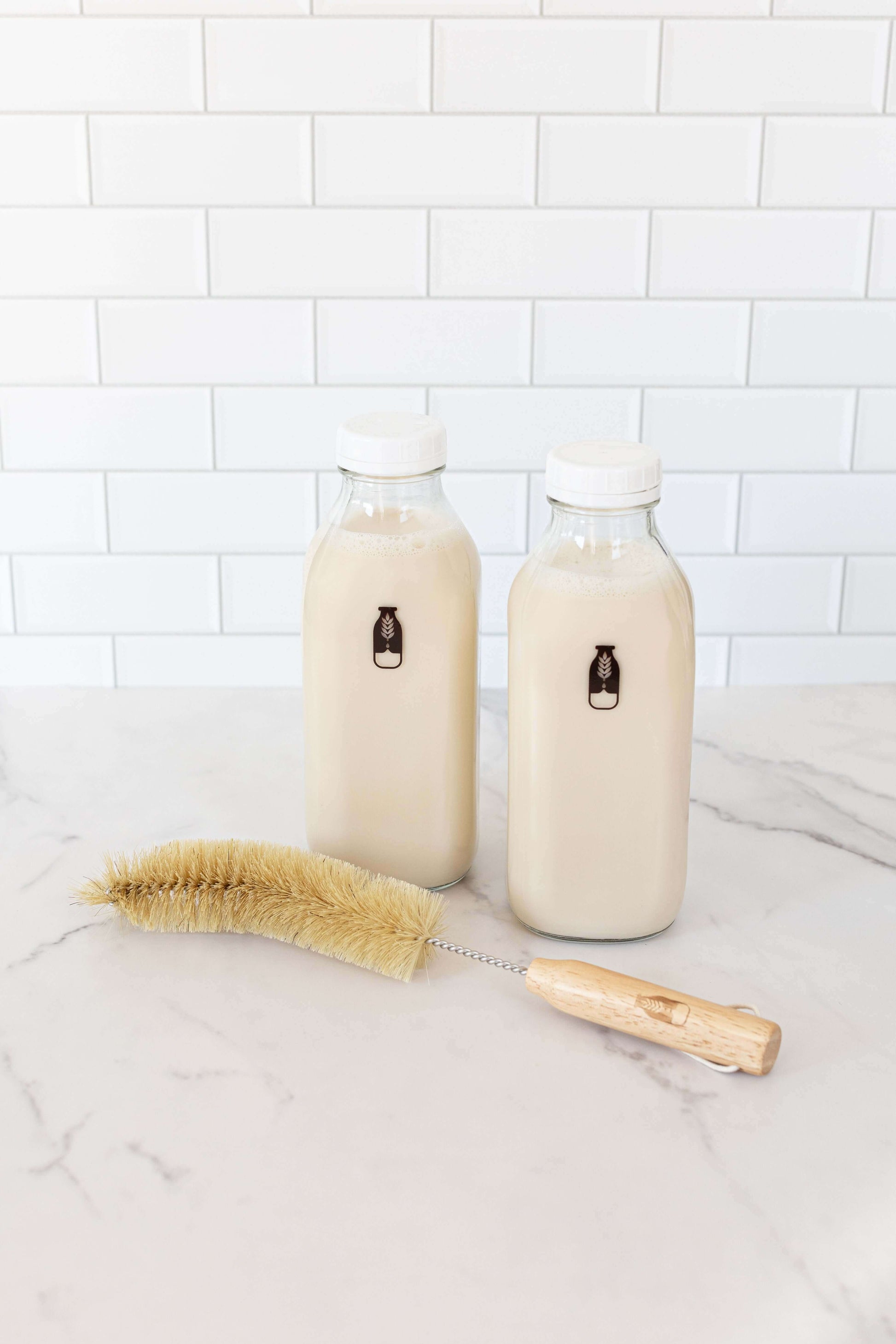 Two Mylky glass bottles filled with milk and a wooden brush